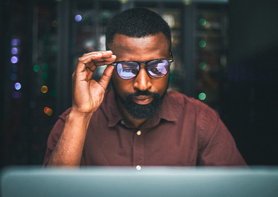African American black male adjusting glasses as he looks down at computer monitor.